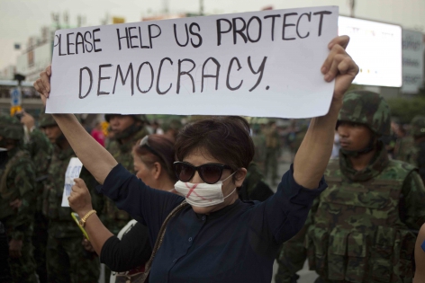 Bangkok, Thaïlande, Mai 2014 Une manifestante anti-coup d'Etat interpelle des journalistes étrangers et s'affiche avec cette banderole devant les soldats postés sur la place de Democracy Monument. ‟S'il vous plaît, aidez nous a protéger la démocratie‟.